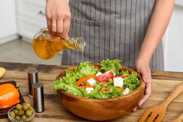 Woman adding olive oil into bowl with tasty salad at table in kitchen