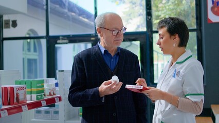 Obraz premium Elderly man in chemist store asking pharmacist for medical opinion, needing treatment for headache. Certified druggist helping senior client choose best pharmaceutical cure for his pain