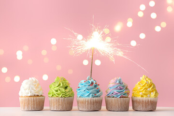 Tasty birthday cupcakes with sparkler on color background