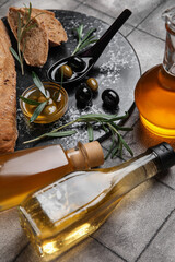 Bottles of oil and olives on grey tile background