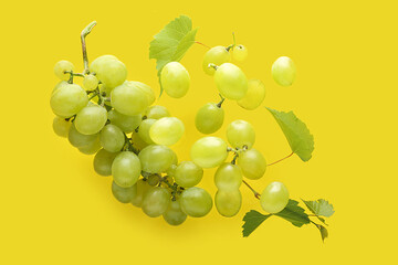 Flying sweet green grapes with leaves on yellow background