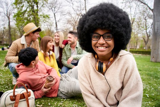 Portrait of young happy smiling afro black girl looking at the camera. Portrait of multiracial group of students hugging and sitting down in the grass. Cheerful female colleague posing outdoors