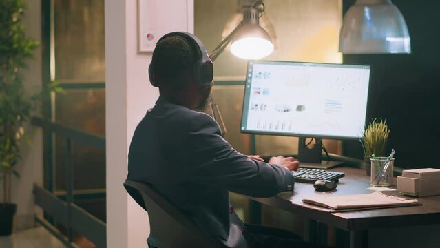 Employee enjoying music, bopping his head to rythm while solving company project tasks during nightshift. Bookkeeper in office with headphones on looking through financial business documents