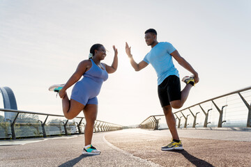 Smiling african american woman and man giving high five doing stretching exercise outdoors on street