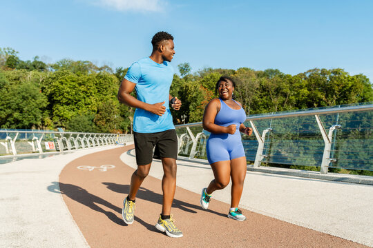 Young african american couple man and plus size woman running together on street exercising outdoors