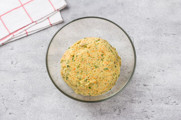 Dough for vegan millet cutlets with carrots, herbs and seeds on a gray textured background, top view. Stage of cooking healthy homemade food