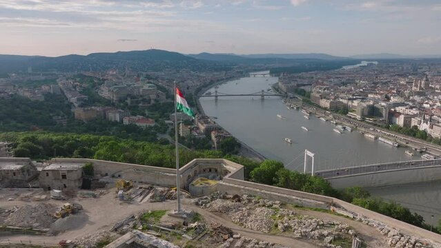 Fly over historic fortification on top of Gellert Hill. Hungarian flag waving on Citadella high above wide river Danube in city. Budapest, Hungary