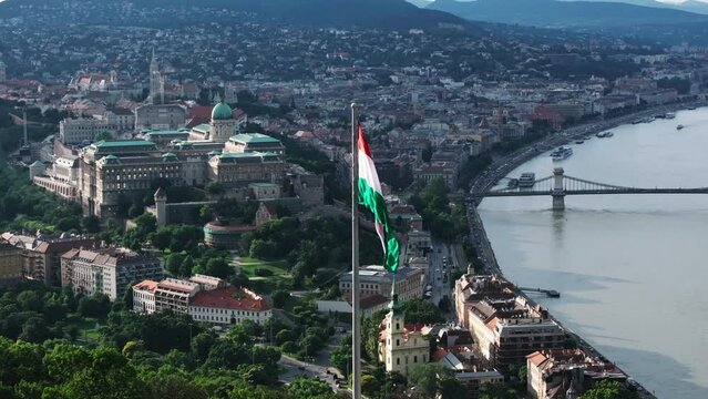Hungarian national flag waving in wind on pole. Sights in background. Buda castle, bridges over Danube and famous parliament building. Budapest, Hungary