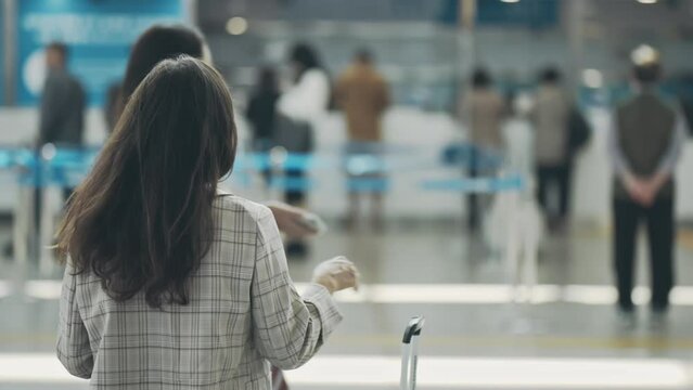 Woman standing back in crowd passenger walking with a yellow suitcase luggage at airport terminal surfing in internet checking her flight, Woman on way to flight boarding gate, Tourist journey concept