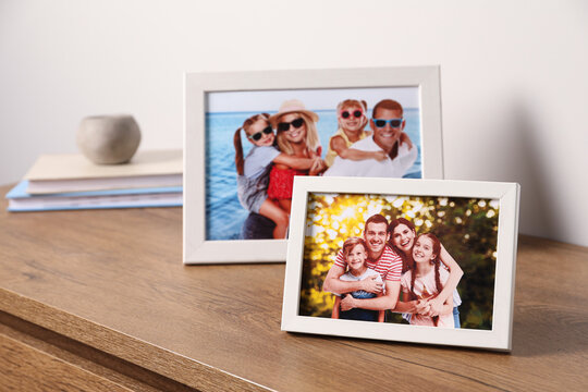 Frames with family photos on wooden table near white wall