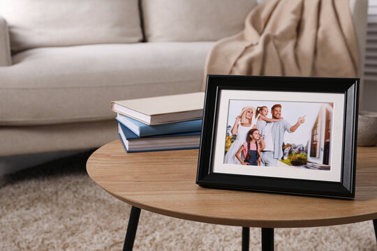 Frame with family photo and stack of books on wooden coffee table in room, space for text