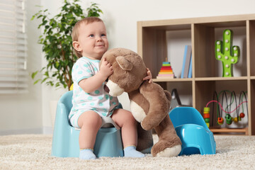Little child and teddy bear sitting on plastic baby potties indoors