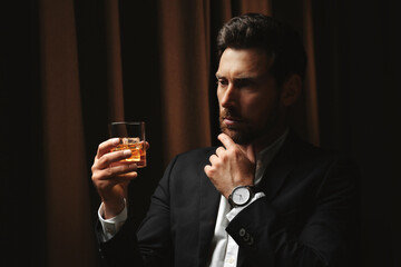 Man in suit holding glass of whiskey with ice cubes on brown background