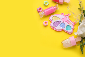 Decorative cosmetics for kids. Eye shadow palette, lipsticks, accessories and flowers on yellow background, closeup. Space for text