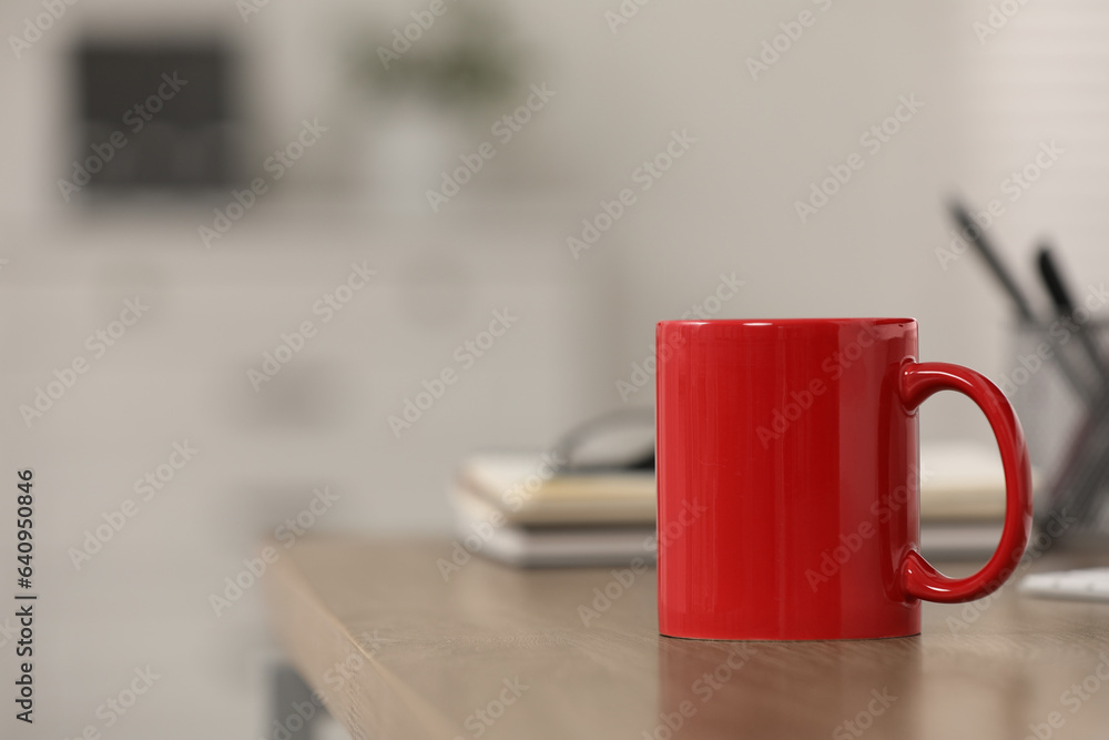 Poster Red ceramic mug on wooden table at workplace. Space for text