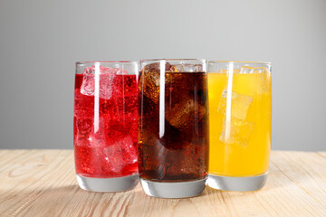 Glasses of different refreshing soda water with ice cubes on wooden table