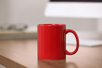 Red ceramic mug on wooden table at workplace