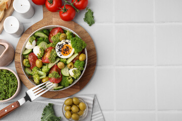Delicious salad with pesto sauce in bowl, ingredients and fork on white tiled table, flat lay. Space for text