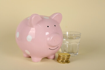 Water scarcity concept. Piggy bank, coins and glass of drink on beige background
