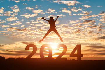 Silhouette of woman jumping to Happy new year 2024 in sunset or sunrise background.