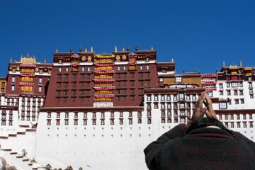 In Lhasa, Tibet, a devoted pilgrim performs a reverent circumambulation before the Potala Palace,...