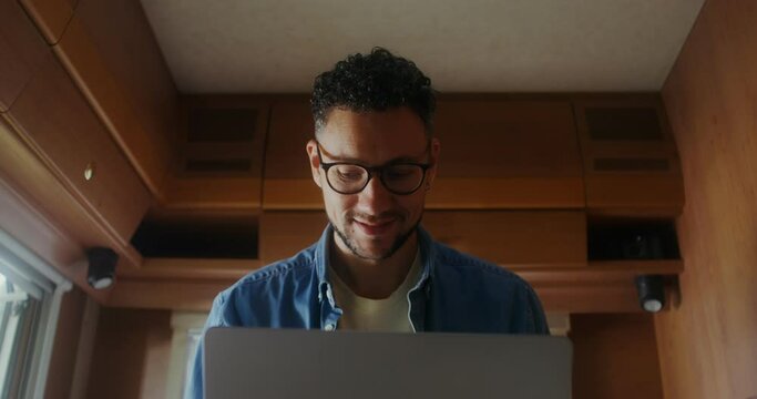 A young man with glasses closes his laptop finishing work sitting in a van, he smiles