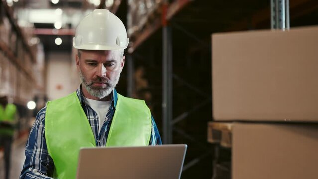 Project Leader is Standing with Laptop Computer and Checking Work Data. Engineers Work Around Him. Factory Worker Engaged in Project Development Using a Laptop Computer
