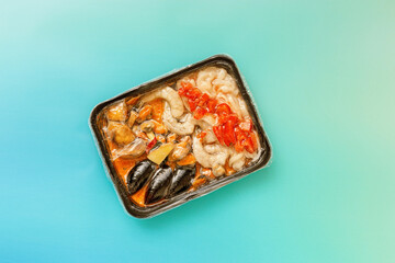 Frozen tom yum soup, semi-finished product in plastic bags on blue teal gradient background. Spicy asian food for cooking home. Plastic package. Seafood, vegetable ingredients for homemade soup