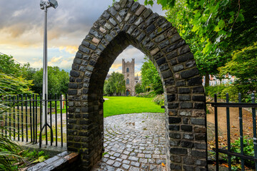 Fototapeta premium The medieval St Audoen's Church can be seen from a stone arch entrance St Audoen's Park in the historic center of Dublin, Ireland.