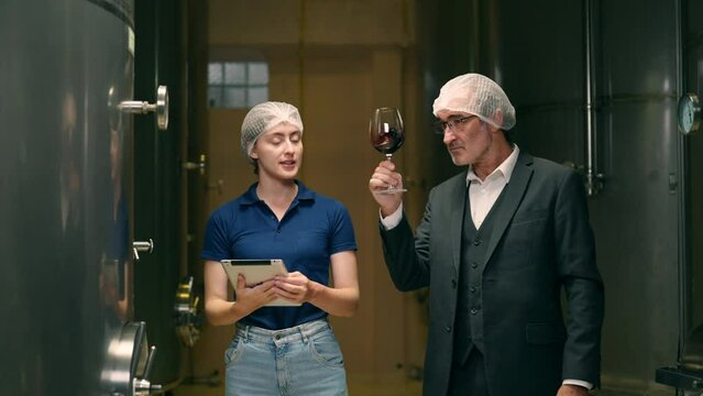 Professional man and woman winemaker inspecting red wine quality in wine cellar and stainless steel barrel in wine factory. Winery, wine shop, brewery liquor manufacturing industry business concept.