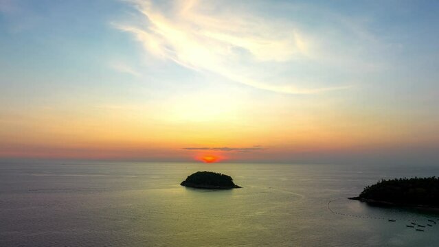 .Aerial hyperlapse The sun slowly sets over the horizon in the ocean.The sky is painted with streaks of yellow and orange..The fading light casts a gentle glow on the waves.Pu island in the vast sea.