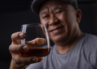 Asian senior man Hand holding glass of whiskey on black background