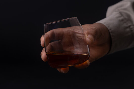 Hand holding glass of whiskey on black background