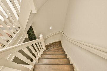 some stairs in a house with white railings and wood flooring on the bottom right handrail, leading up to the top