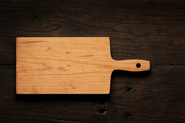 Handmade cherry wood cutting board on black solid wood table top. Empty wooden chopping board background.