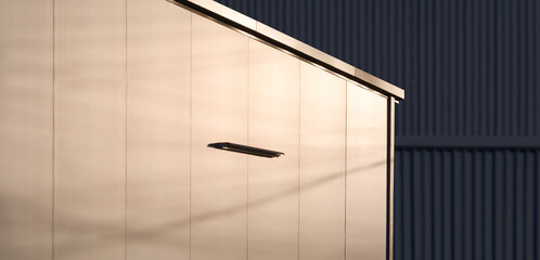 Sunlight reflection on surface of aluminium composite wall of industrial office building with blurred background of black corrugated warehouse wall in evening time