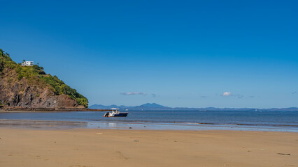 Fototapeta na wymiar Sandy beach on a tropical island. The boat is moored in the blue ocean. The white building on the hill. A mountain range against the azure sky on the horizon. Madagascar. Nosy Be island.
