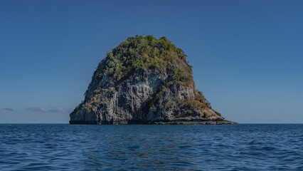 Naklejka premium A lonely island rises in the blue ocean. There is green vegetation on steep rocky slopes. Clear azure sky. Madagascar. Nosy Kivinjy
