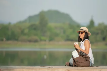 Foto op Canvas asian woman traveler with backpack and cup of coffee sitting on quayside relax during coffee break on background summer vacations and lifestyle hiking concept. © nareekarn