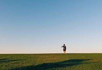 Fototapeta premium Man running up the green hill on the horizon, minimalist landscape