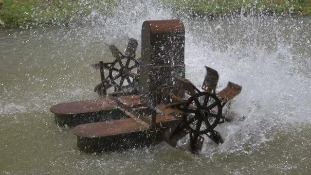 Old rusty electric turbine is adding oxygen in to the water. Aeration turbine rotating wheel paddles for increasing water quality in the canal. Splashing water. Slow motion.