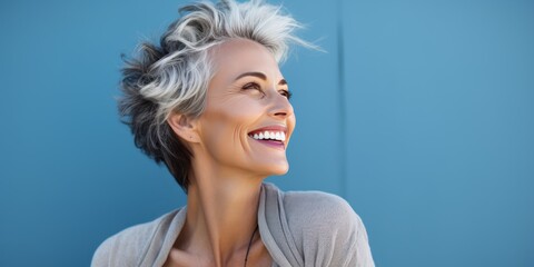 Psychology portrait of a happy smiling Scandinavian woman in her 50s. Luxurious middle-aged woman with a short gray hairdo looking at copy space. Photo on blue background.