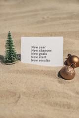 NEW YEAR CHANCES GOALS START RESULTS text on paper greeting card on background sandy beach sun coast. Christmas balls Santa hat New Year New Me Resolutions decoration. Summer vacation decor. Holiday