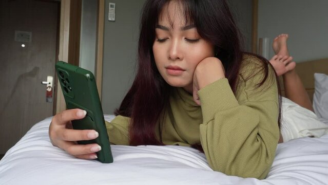 Asian woman laying on bed while scrolling on her phone