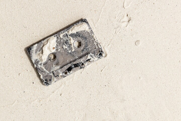 Used audio cassette lays on wet white sand
