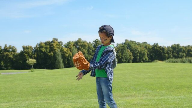 Side view of motivated determined cute school age black boy pitcher wearing eye black and baseball glove, throwing ball while playing baseball game on green grass field.