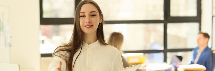 A beautiful woman in office holds out a hand for greeting