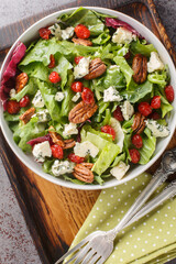 Vegetarian salad with leaf lettuce, spinach, arugula, dried cherries, gorgonzola cheese, pecans dressed with vinaigrette sauce close-up in a bowl on the table. Vertical top view from above