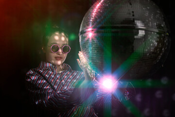 A beautiful girl in stylish glasses is spinning a sparkling disco ball.