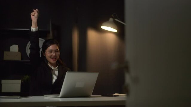 Tired woman looking at laptop working hard sleepy in the dark room office. Stressed asian business woman working late at night in the office hands on head feeling headache. Overtime concept.